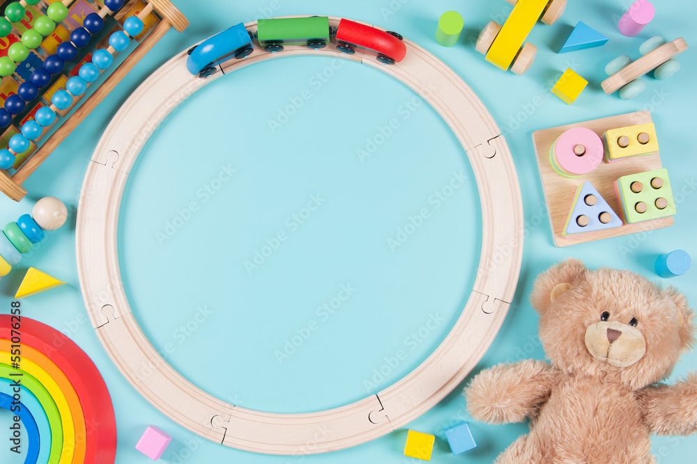 Obraz premium Baby kids toys frame background. Teddy bear, wooden educational stacking color recognition puzzle toys, wooden train, abacus and colorful blocks on light blue background. Top view, flat lay