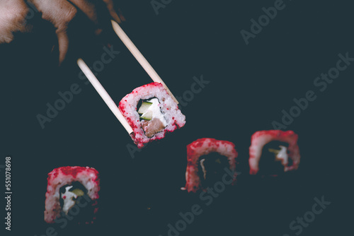 Female hand takes california sushi rolls with Chinese chopsticks. Selective focus, black background