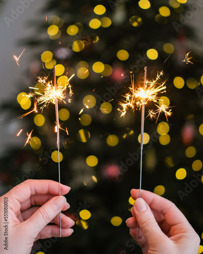 Bengal lights in female hands on the background of the Christmas tree. Happy New Year. Celebration atmosphere