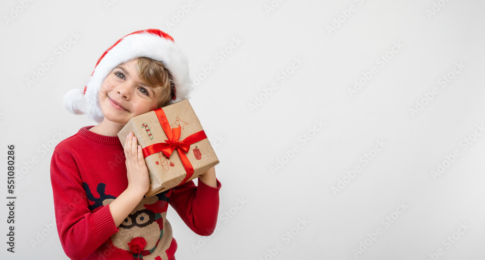 Obraz premium Excited funny dutch caucasian child girl boy wear red Santa hat holding Christmas gift boxes dreaming over white background. Copy space. Merry Christmas presents shopping sale.