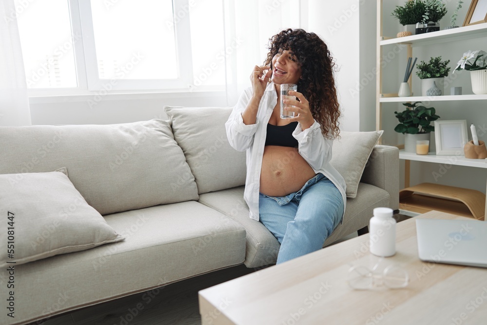Pregnant woman smile blogger takes vitamins and medicines pills with a glass of water close-up sitting on the sofa at home freelancer in the last month of pregnancy lifestyle before childbirth Pregnant woman smile blogger takes vitamins and medicines pills with a glass of water close-up sitting on the sofa at home freelancer in the last month of pregnancy lifestyle before childbirth