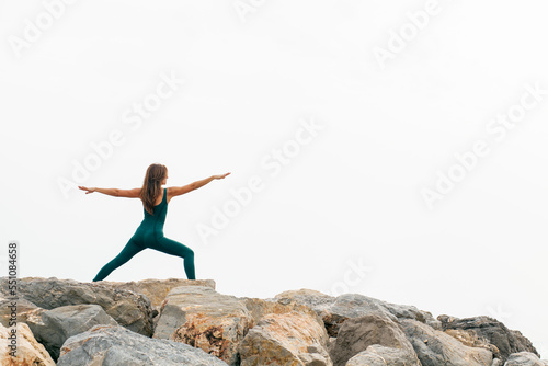 Peaceful focused woman standing in Warrior Two exercise yoga, Virabhadrasana 2 pose, wearing green sportswear. Working out, full length. Outdoor training. No stress and health care concept...