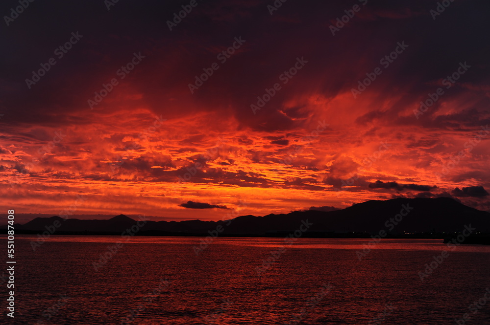 Red, pink, orange and violet sunrise at the seaside during dawn with clouds in the sky and mountains on the shore of a port