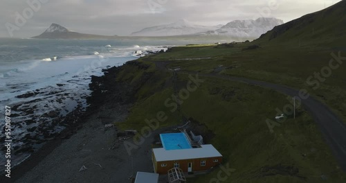 aerial view of Krossneslaug geothermal pool on coast of greenland sea in iceland with green grass and moutnains with snow  in wesfjords photo