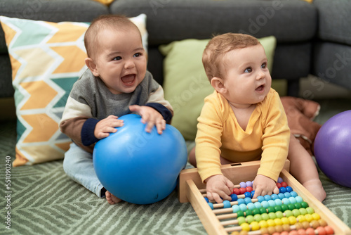 Two toddlers playing with balls and abacus sitting on floor at home