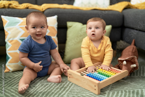 Two toddlers playing with abacus sitting on floor at home