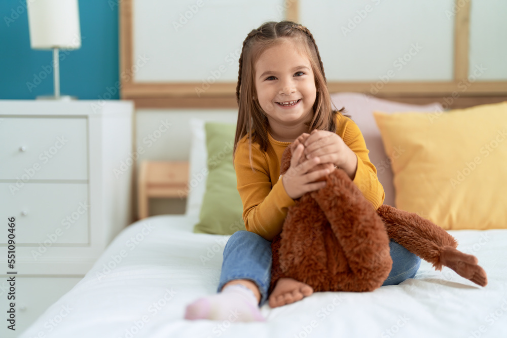 Adorable hispanic girl hugging monkey doll sitting on bed at bedroom Adorable hispanic girl hugging monkey doll sitting on bed at bedroom