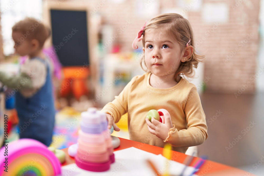 Naklejka premium Adorable hispanic girl playing with hoops game sitting on table at kindergarten