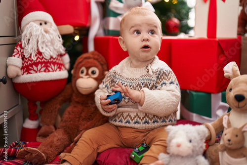 Adorable caucasian baby playing with car toy sitting on floor by christmas gifts at home