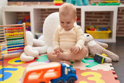 Adorable caucasian baby playing with car and truck toy sitting on floor at kindergarten