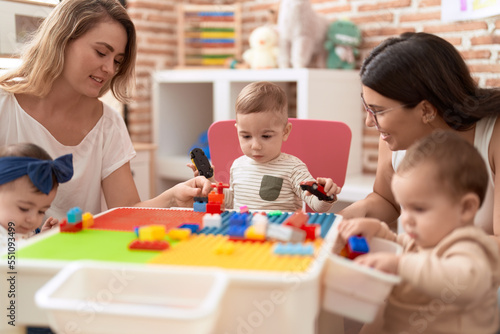 Teachers and preschool students playing with construction blocks sitting on table at kindergarten