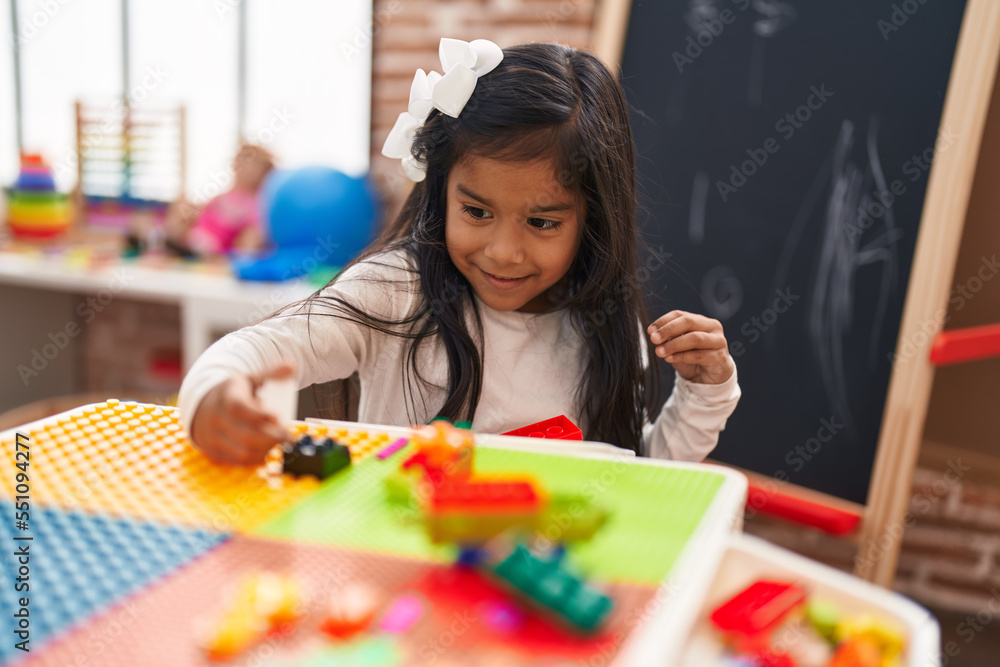Adorable hispanic girl playing with construction blocks sitting on table at kindergarten Adorable hispanic girl playing with construction blocks sitting on table at kindergarten