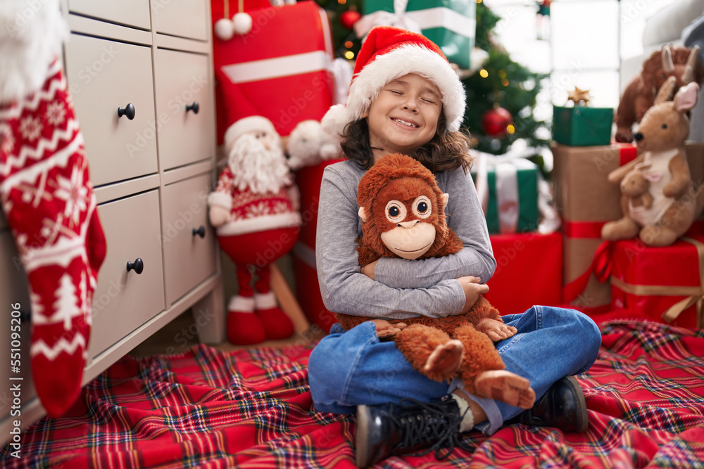 Adorable chinese girl hugging monkey doll sitting on floor by christmas tree at home Adorable chinese girl hugging monkey doll sitting on floor by christmas tree at home