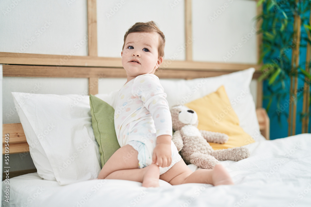 Adorable caucasian baby sitting on bed with relaxed expression at bedroom Adorable caucasian baby sitting on bed with relaxed expression at bedroom