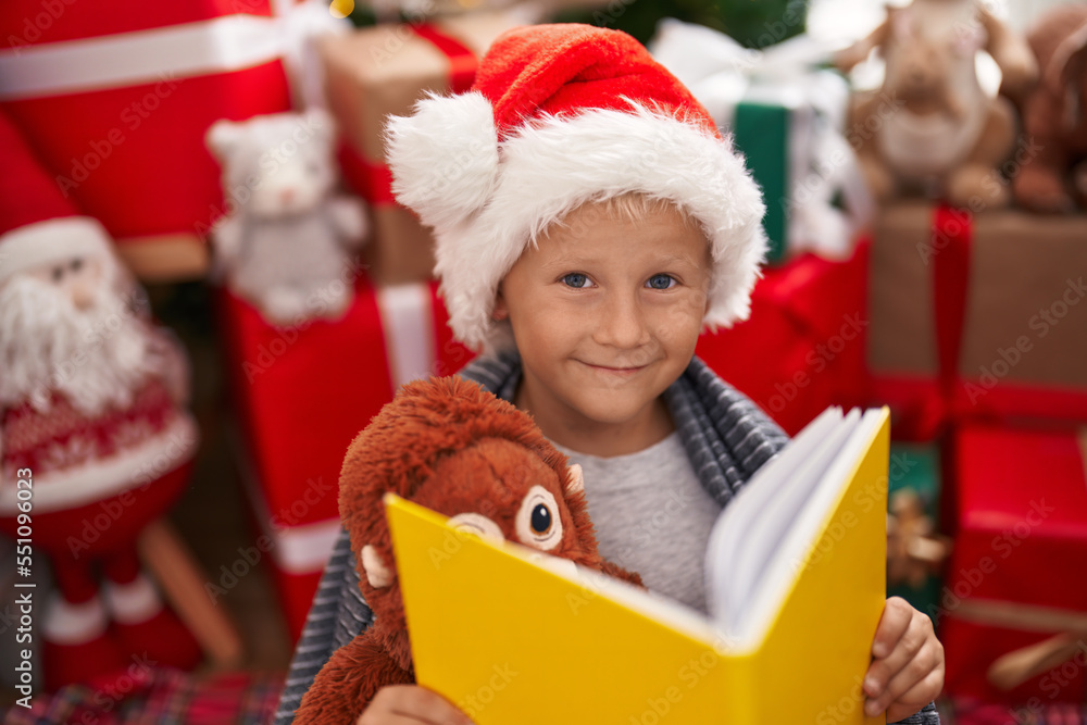Adorable toddler reading book sitting by christmas tree at home