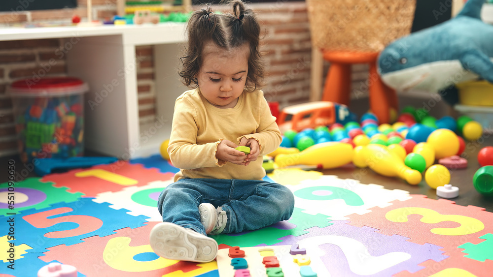 Adorable hispanic girl playing with maths puzzle game sitting on floor at kindergarten Adorable hispanic girl playing with maths puzzle game sitting on floor at kindergarten