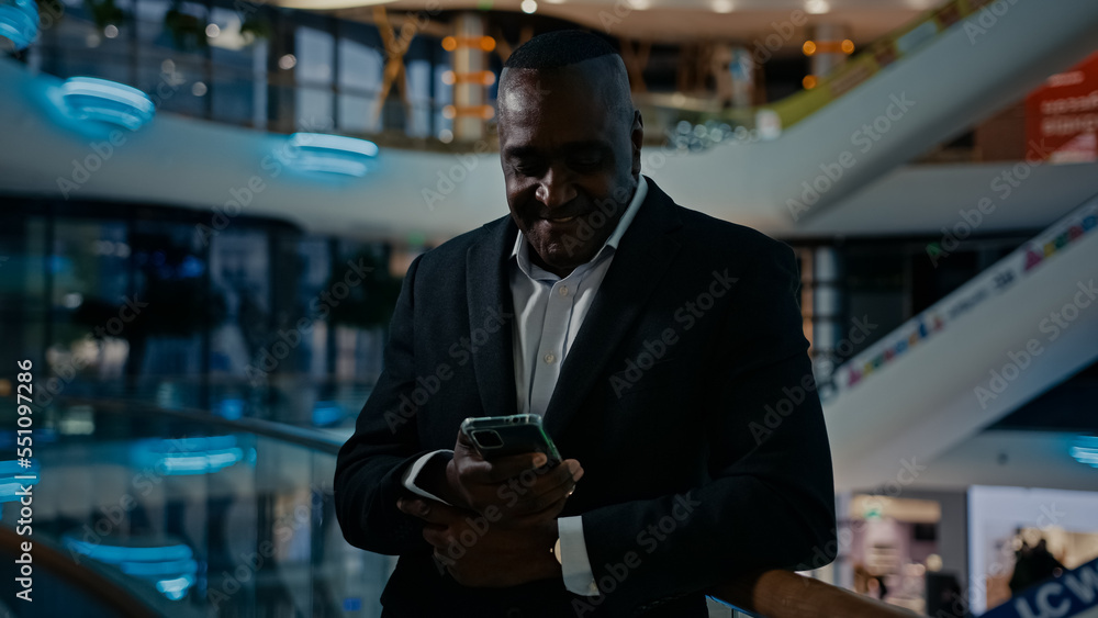 African American businessman standing in shopping mall company office looking at mobile phone screen talk has video call smartphone conference talking discussing friendly smile answer cellphone chat