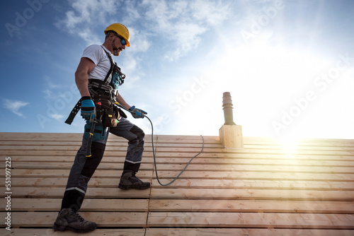 Foto A roofer with a safety harness and tool belt standing on the roof