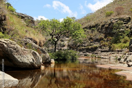 Small valley with a stream of calm waters  between rocks and vegetation. Region of Concei  ao de Mato Dentro in Minas Gerais  Brazil