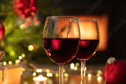 Christmas celebration. Red wine glasses, Xmas presents and decoration on table, fireplace background. Xmas celebration
