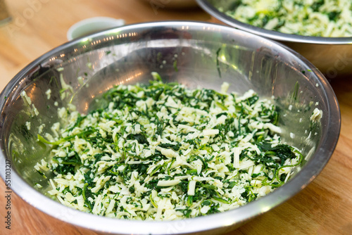 A bowl of grated cheese mixed with chopped herbs. The filling for the cheese pie.