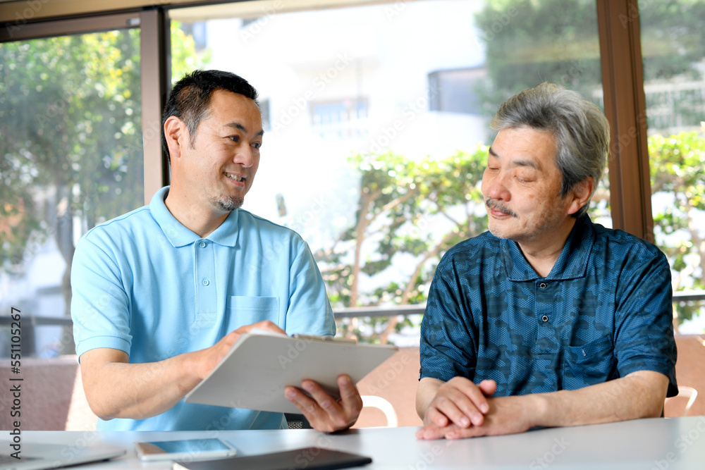 高齢者男性に説明をする男性の介護士
高齢者男性に説明をする男性の介護士