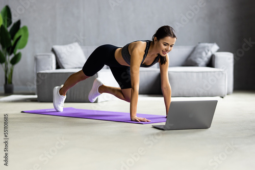 Tablou canvas Fit woman doing yoga plank and watching online tutorials on laptop training in l