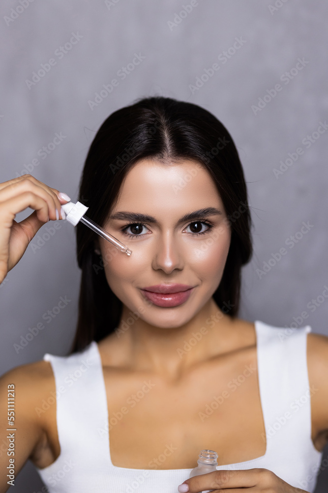 Obraz premium Portrait of young woman applying hyaluronic acid at home. Skin care routine.
