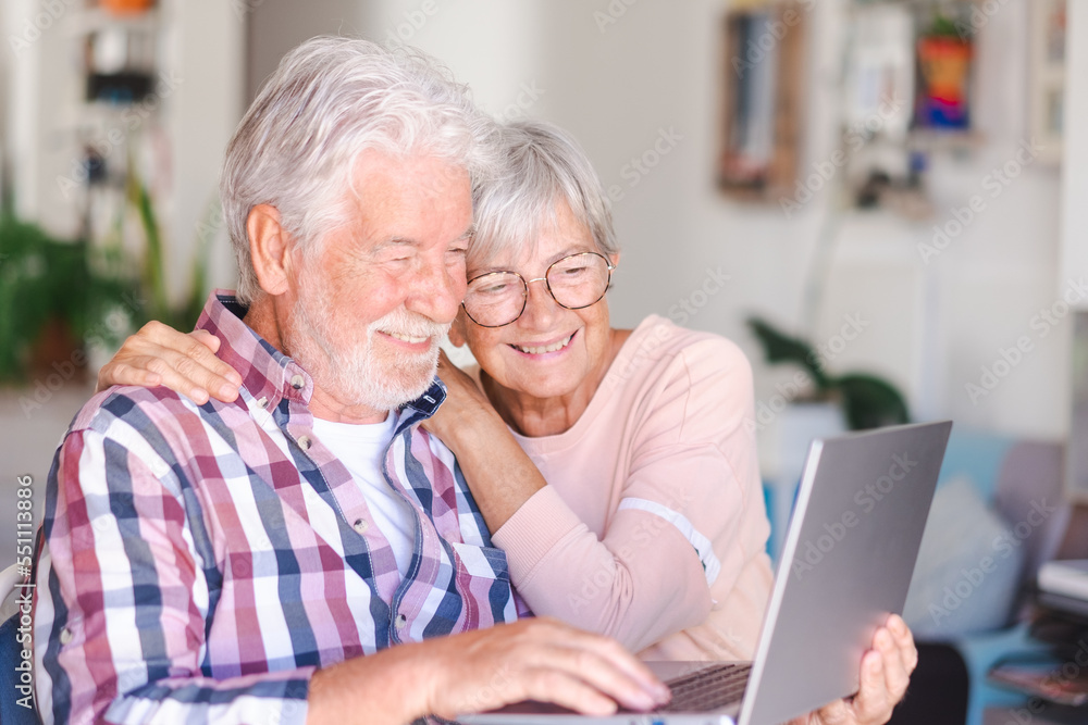 Portrait of happy modern elderly couple browsing together on laptop at home. Joyful and beautiful senior couple white haired enjoying technology and social media
