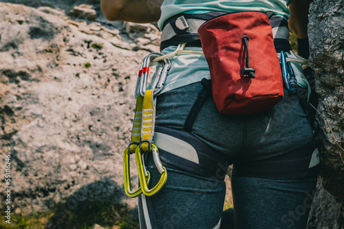 Close-up on a woman wearing a harness with climbing equipment like tube, hms carabiner, chalk bag, quickdraws. climber prepers to belay his partner or to start climbing on a rock wall