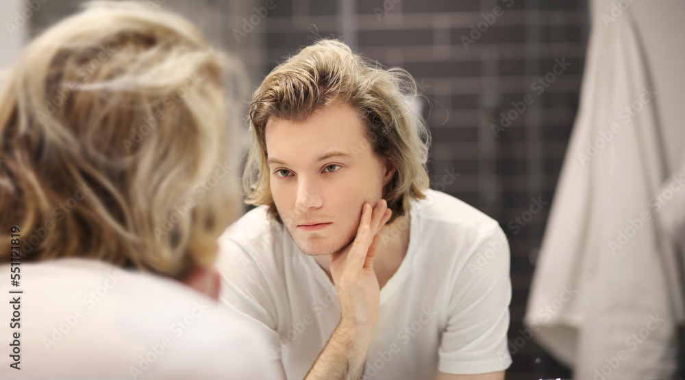 young man looking in the mirror,combing his hair,looking at problems on face. young man looking in the mirror,combing his hair,looking at problems on face.