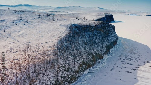 Lake Baikal, winter. Flying over an icy rock overgrown with pine trees. Sunny weather, snow lying around. Baikal, Siberia, Russia. Aerial drone shot 4k photo