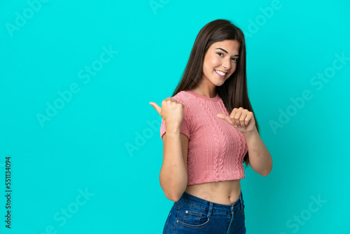 Young Brazilian woman isolated on blue background pointing to the side to present a product