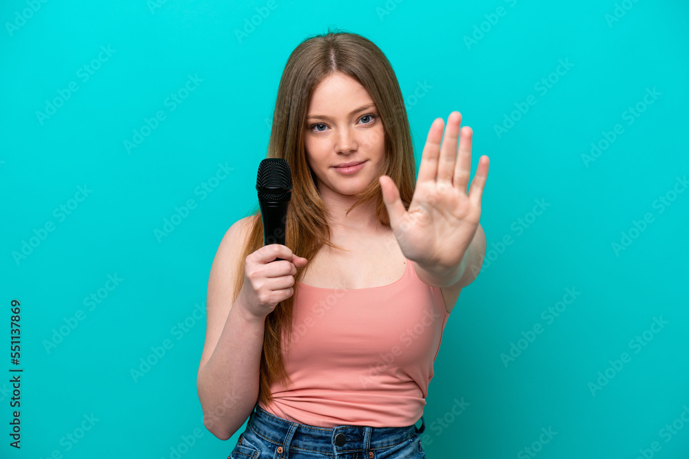 Fototapeta premium Singer caucasian woman picking up a microphone isolated on blue background making stop gesture