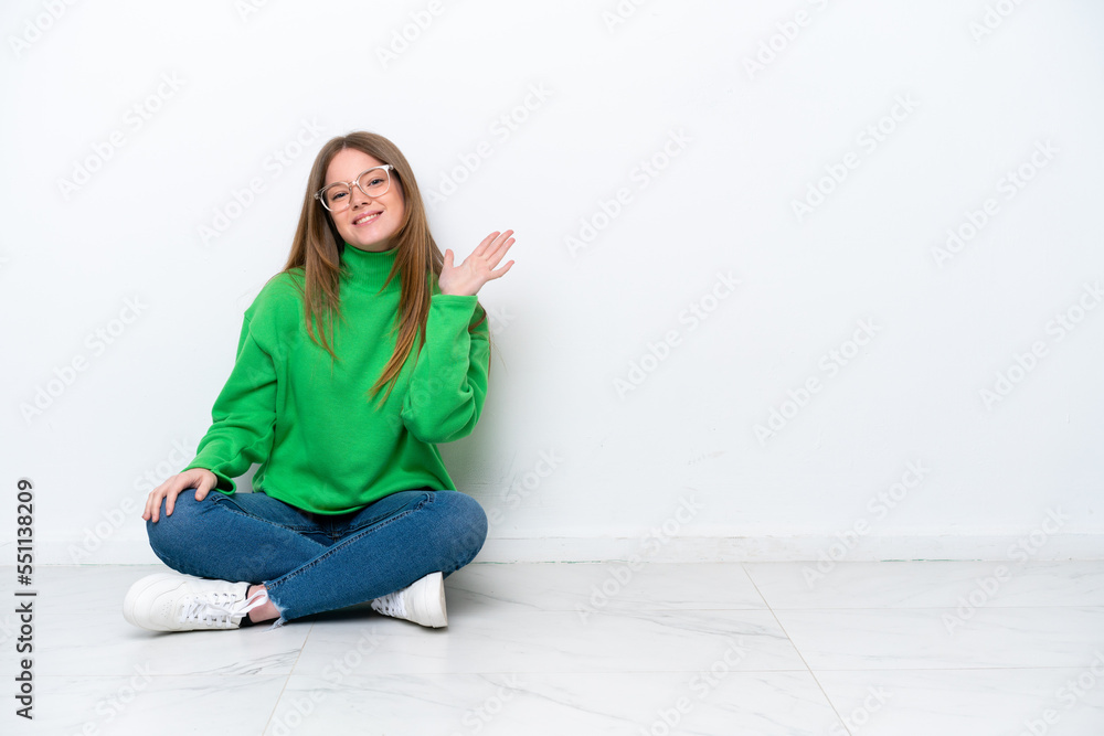 Young caucasian woman sitting on the floor isolated on white background saluting with hand with happy expression Young caucasian woman sitting on the floor isolated on white background saluting with hand with happy expression