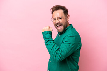 Middle age caucasian man isolated on pink background celebrating a victory