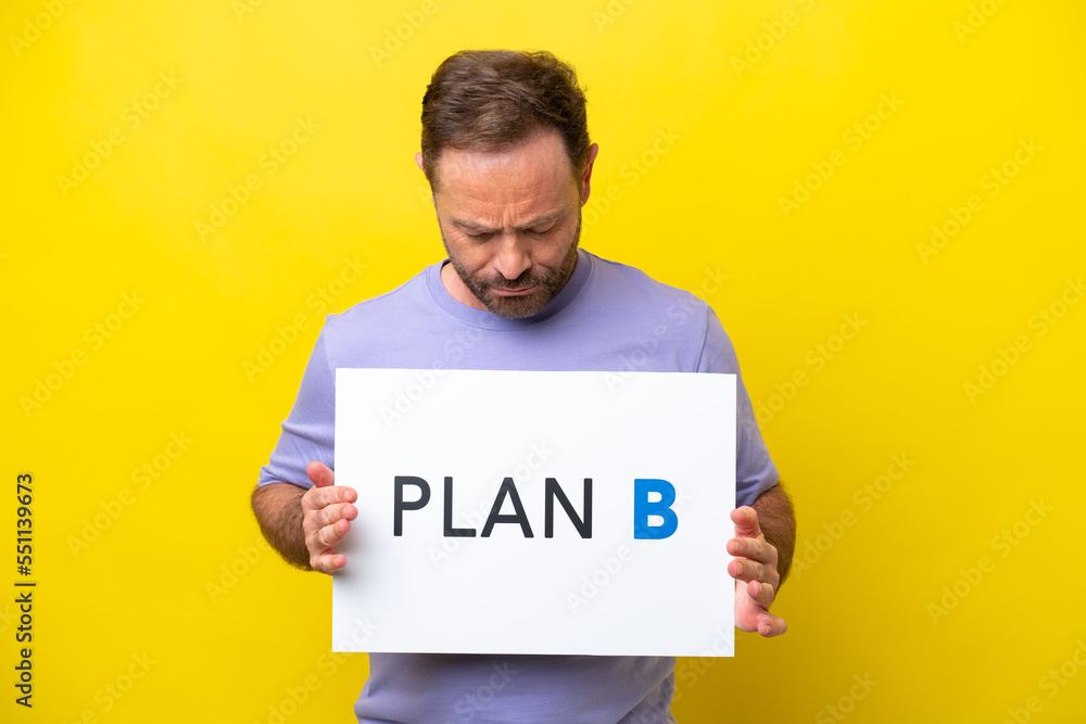 Middle age caucasian man isolated on yellow background holding a placard with the message PLAN B Middle age caucasian man isolated on yellow background holding a placard with the message PLAN B