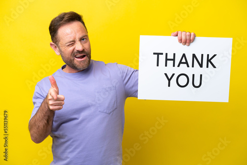 Middle age caucasian man isolated on yellow background holding a placard with text THANK YOU and pointing to the front