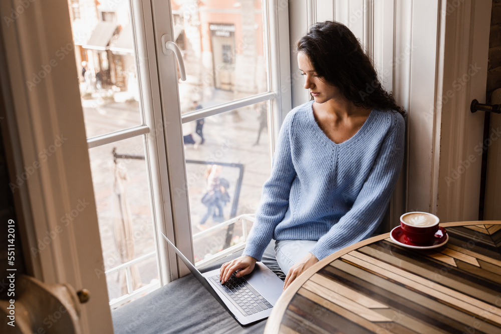 Attractive girl freelancer is working online on laptop and drinking coffee in cafe. Confident business woman manager with laptop is working with colleagues online in cafe. Attractive girl freelancer is working online on laptop and drinking coffee in cafe. Confident business woman manager with laptop is working with colleagues online in cafe.