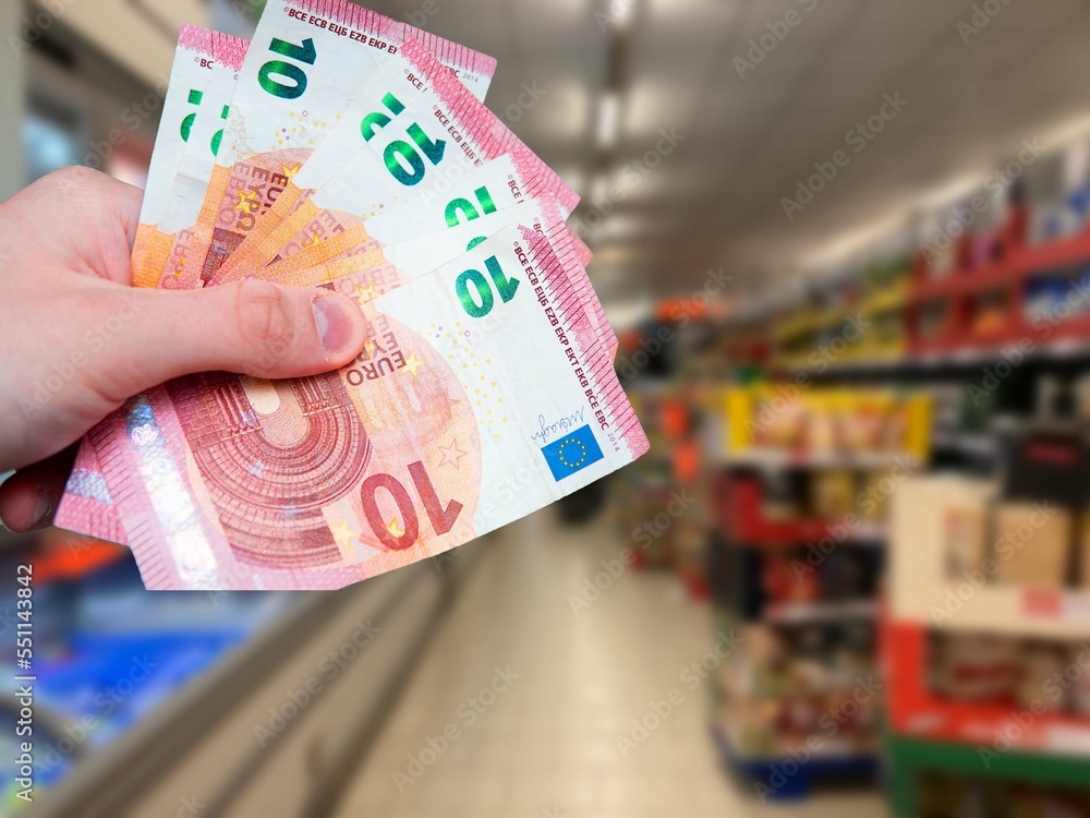 Euro banknotes in hand and grocery store in the background. Increase in food prices in Europe. Rising inflation