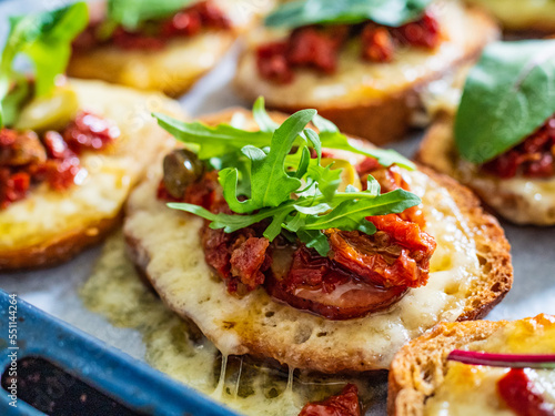 Tasty sandwiches - baked bread with sausage, cheese, sun dried tomatoes and greens on wooden table 
