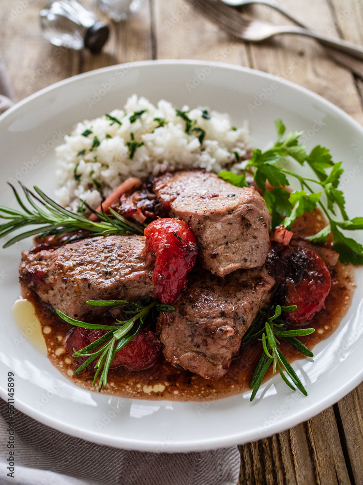 Roast pork loin with plums in sauce and white rice on wooden table
