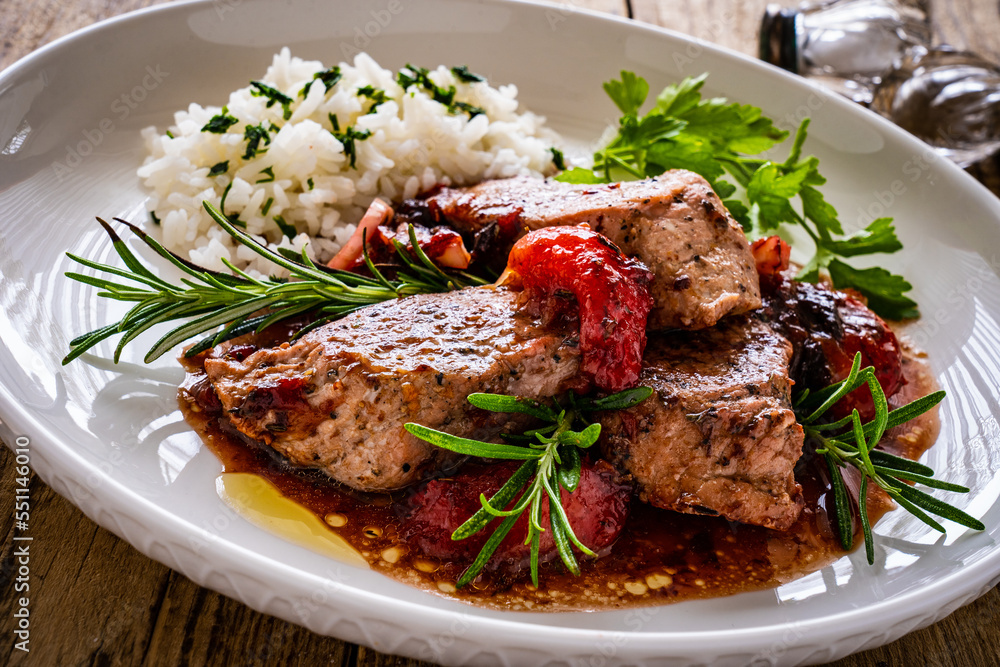 Roast pork loin with plums in sauce and white rice on wooden table
