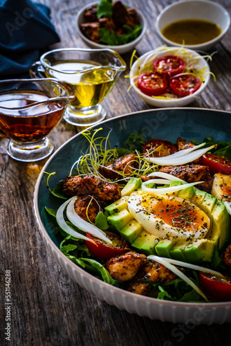 Tasty salad - fried chicken breast, avocado, boiled eggs, mini tomatoes and fresh green vegetables on wooden background 