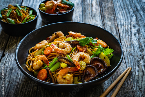 Mie noodles with fried prawns, shiitake mushrooms, coriander, carrot and celery on wooden table 