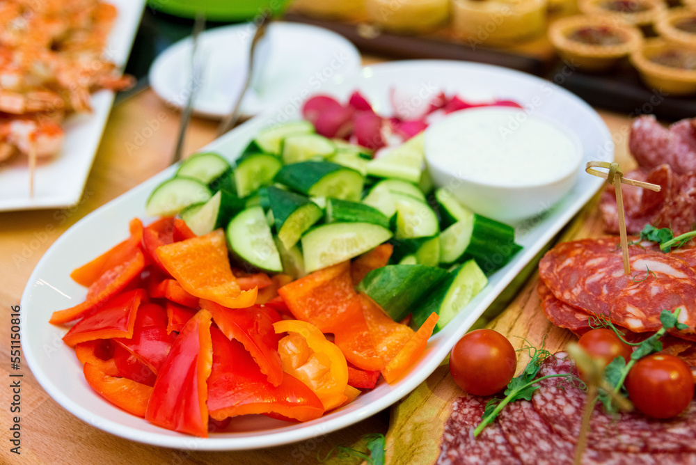 A plate of fresh sliced vegetables: red bell pepper, cucumber, radish, and a bowl of sauce