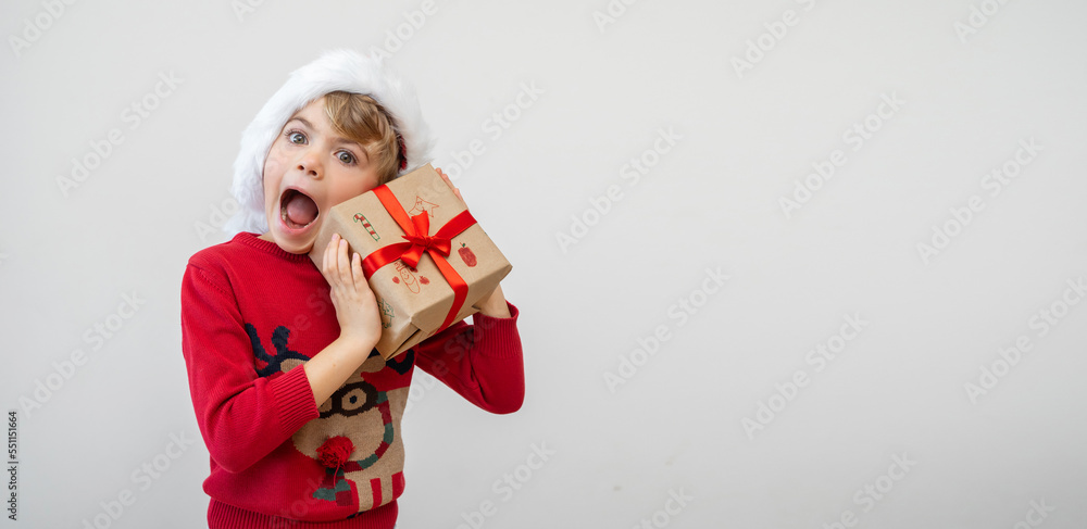 Obraz premium Excited funny Canadian caucasian child girl boy wear red Santa hat holding Christmas gift boxes dreaming over white background. Copy space. Merry Christmas presents shopping sale.