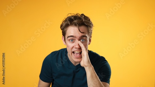 Portrait of caucasian hipster man 20s looks around put hand to mouth shh, quiet, tells secret isolated on yellow background studio portrait