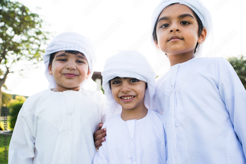 Cute middle eastern kids wearing traditional arab clothing playing and having fun in a park outdoors Cute middle eastern kids wearing traditional arab clothing playing and having fun in a park outdoors