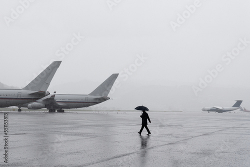 A man under an umbrella at the airport. Desert airfield. Rainy weather at the airport. Large airfield with aircraft. The man goes to the plane.